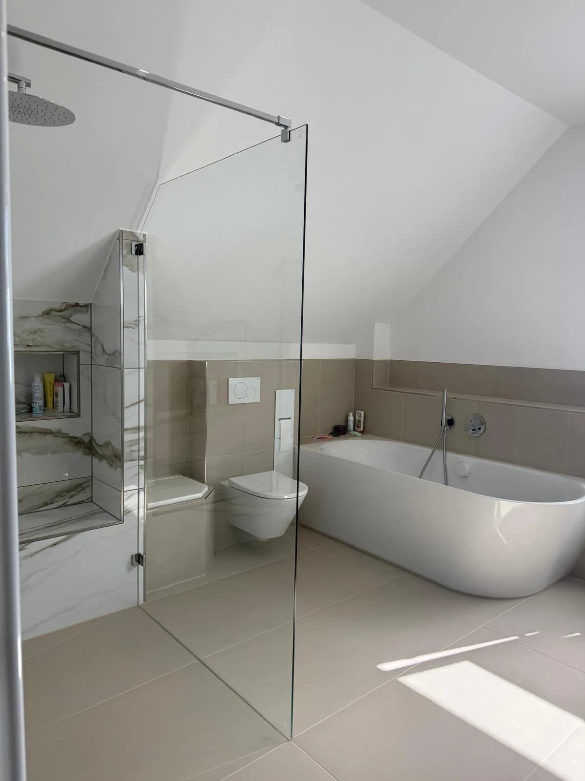 Blick durch die Glasabtrennung der bodengleichen Dusche auf WC und freistehende Badewanne