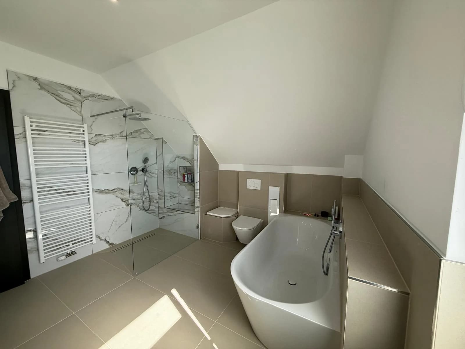 Fertiggestelltes Badezimmer im Dachgeschoss mit bodengleicher Dusche in Marmoroptik, freistehender Badewanne und wandhängendem WC